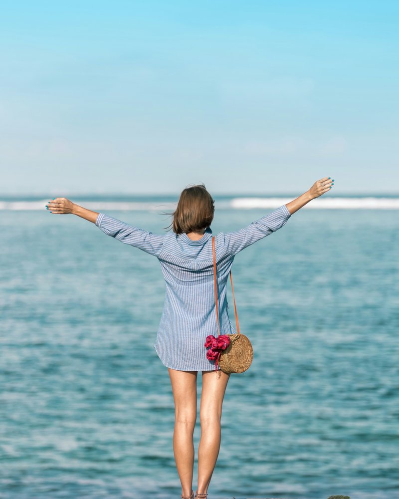 Woman at the ocean with arms raised, feeling free and energized